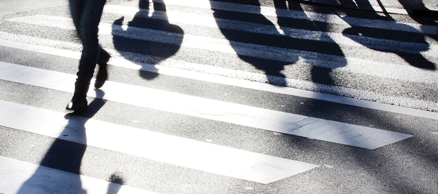 Shadows of people walking on a crosswalk on a busy city street